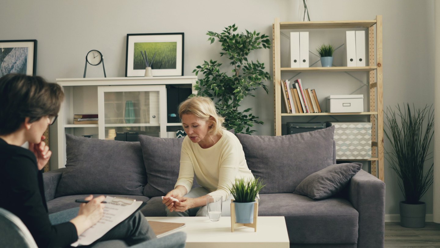 Therapeutin macht sich Notizen, während ein verzweifelter Klient auf dem Sofa sitzt.